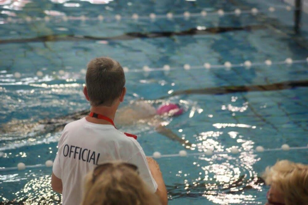 Een redder en wedstrijdofficial kijkt naar een zwemmende persoon.